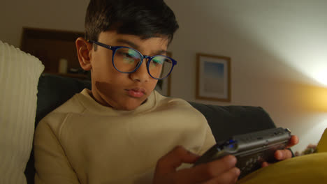 Young-Boy-Sitting-On-Sofa-At-Home-Playing-Game-Or-Streaming-Onto-Handheld-Gaming-Device-At-Night-1